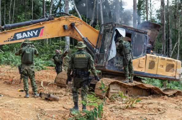 Grupo de homens vestidos com uniformes de camuflagem do IBAMA destrói escavadeira na floresta amazônica