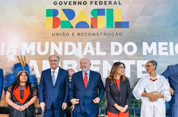 O Presidente Lula e o Vice Alckmin, junto com ministras e ministros, diante de um cartaz sobre o Dia Mundial do Meio-Ambiente