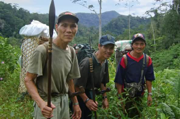 Três homens indígenas com cestas nas costas na floresta tropical malaia