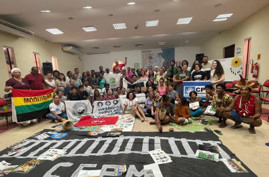 Foto de grupo de cerca de 50 pessoas com faixas em uma sala de seminário. Uma das faixas traz o desenho de um trilho de trem.
