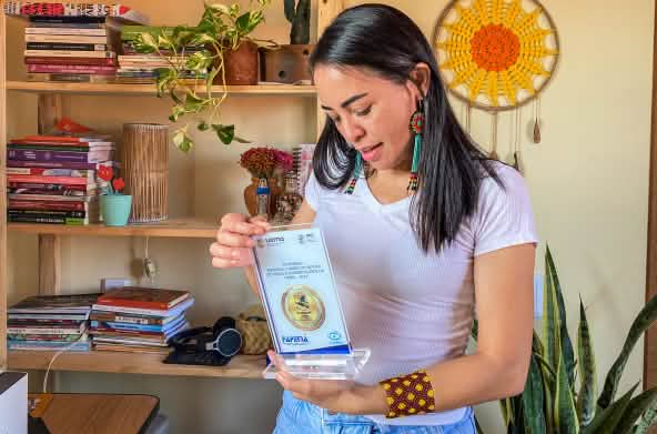 Mulher segura uma placa de premiação e a observa