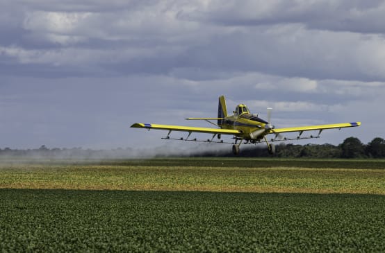 Um avião a hélice pulveriza pesticidas do ar sobre um campo de soja