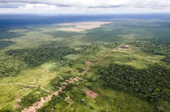 Vista aérea de um pequeno município ao longo de uma pista reta, e na parte de trás, as monoculturas