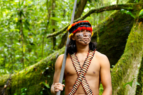 Representante de um povo da floresta com zarabatana, de rosto pintado e enfeitado com uma pena