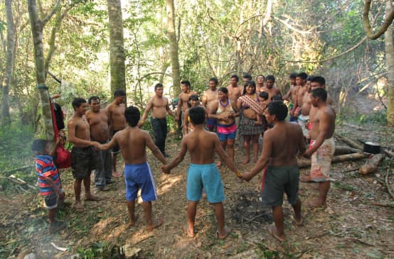 Indígenas Ka'apor - crianças, mulheres e homens - dão-se as mãos e fazem uma roda na floresta tropical