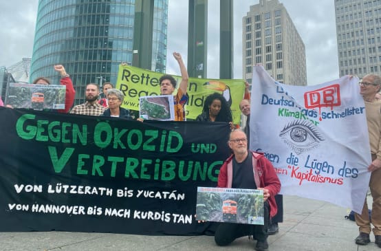 Um grupo de pessoas protesta com grandes faixas coloridas em frente a três torres de escritórios