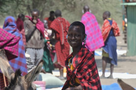 Mulheres e homens do povo Massai com sarongues coloridos em um mercado, uma mulher olha para a câmera.