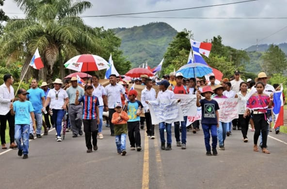 Manifestantes marcham com faixas, bandeiras e guarda-chuvas em uma rodovia no Panamá
