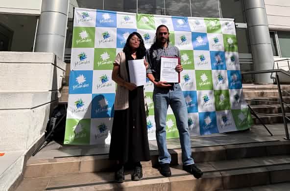 Uma mulher e um homem diante de tela com a inscrição “YASunidos”, em pé diante da entrada de um prédio, com documentos à mão.
