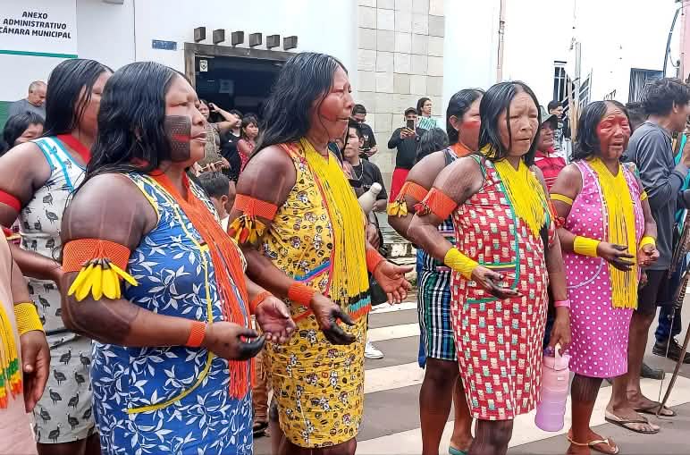 Seis mulheres indígenas com corpos pintados, colares e vestidos coloridos