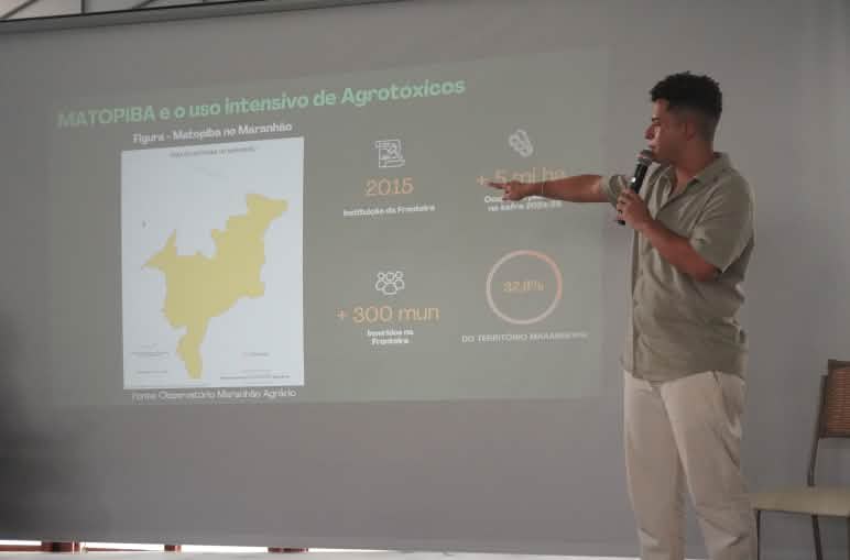 Homem em pé usando microfone aponta no telão imagens com dados sobre uso de agrotóxicos