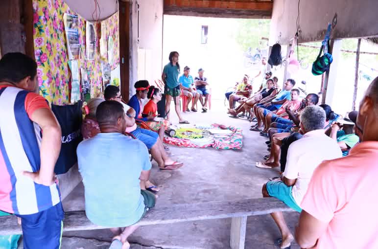 Mulheres e homens conversam sentados em um semi-círculo na varanda de uma casa