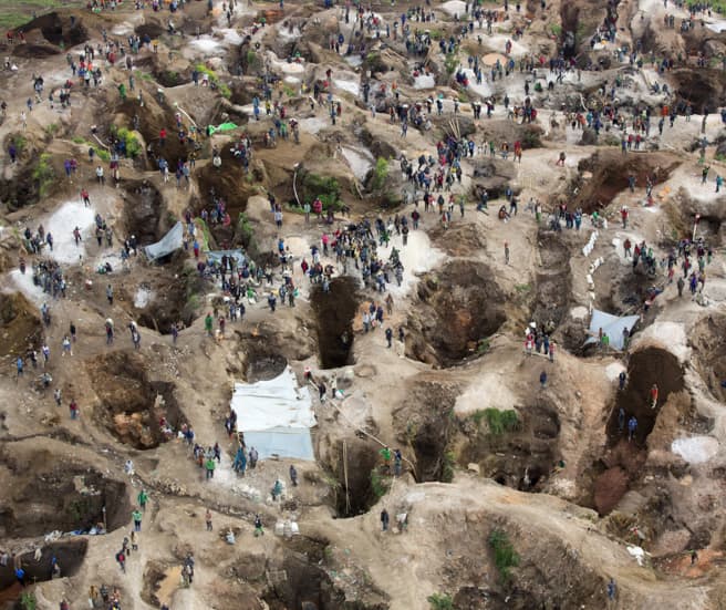 Vista aérea de buracos profundos, em parte preenchidos com água, e entre eles bastante gente.