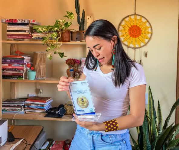 Mulher segura uma placa de premiação e a observa