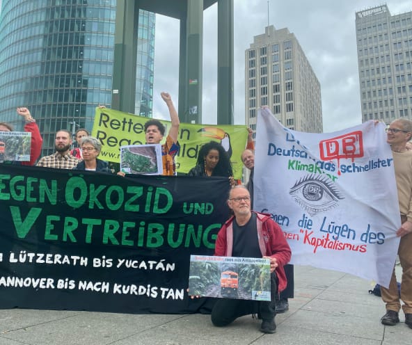 Um grupo de pessoas protesta com grandes faixas coloridas em frente a três torres de escritórios