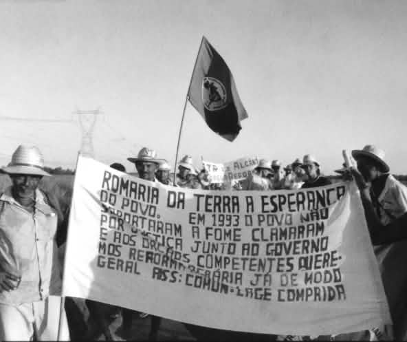 Trabalhadores rurais caminham segurando uma faixa em defesa do acesso à terra