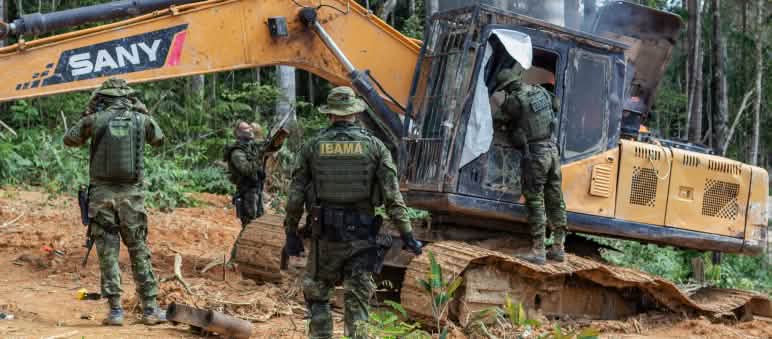 Grupo de homens vestidos com uniformes de camuflagem do IBAMA destrói escavadeira na floresta amazônica