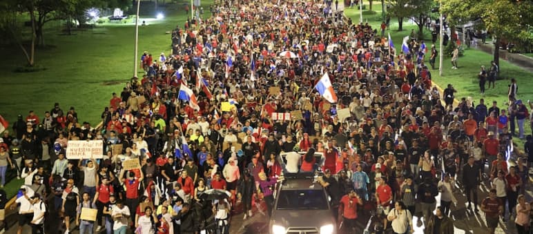 Manifestação com milhares de pessoas passando por uma rua na capital