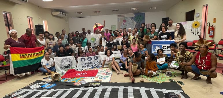 Foto de grupo de cerca de 50 pessoas com faixas em uma sala de seminário. Uma das faixas traz o desenho de um trilho de trem.
