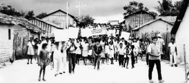 Dezenas de crianças e jovens caminham por área rural com faixas de protesto
