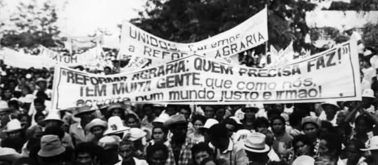 Multidão de pessoas carregam faixas com dizeres a favor da reforma agrária