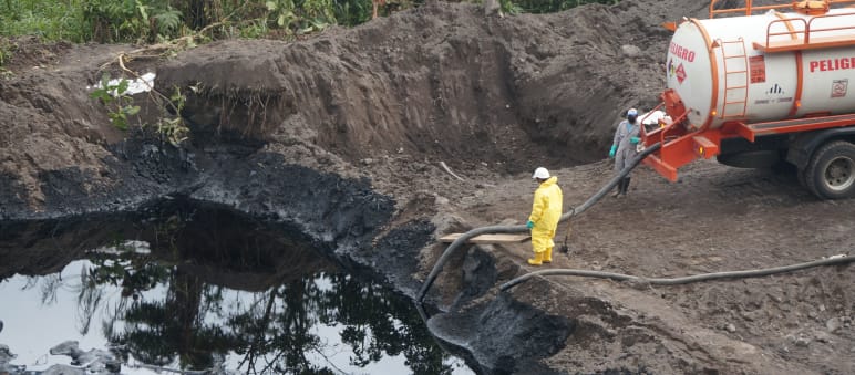 Dois petroleiros transferem petróleo com uma mangueira de um lago coberto de terra para um caminhão-tanque.