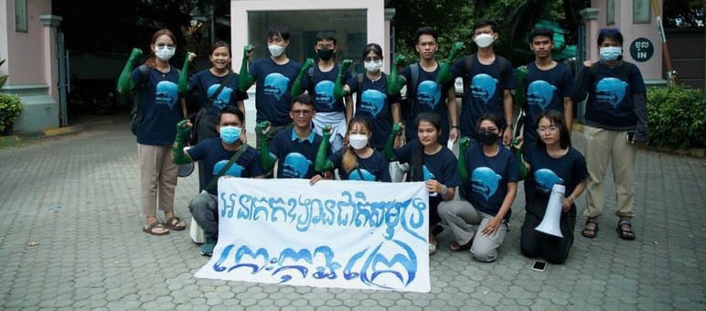 15 adolescentes em pé, à frente do prédio do Ministério do Turismo e a segurar, diante da câmera, uma faixa na qual consta: „Koh Kong Island deve se tornar parque nacional marítimo“