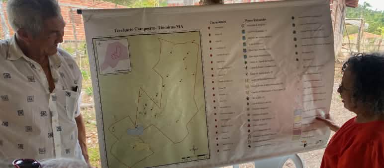 Três pessoas observando o mapa pendurado em um poste de madeira.