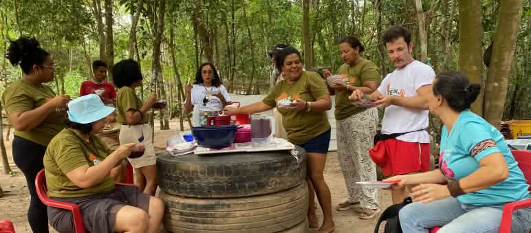 Grupo de 9 pessoas almoçando e conversando em torno de mesa improvisada