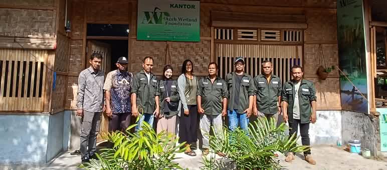 Foto de grupo da equipe da AWF diante de prédio comercial feito de ratã e bambu