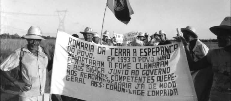 Trabalhadores rurais caminham segurando uma faixa em defesa do acesso à terra