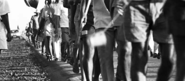 Imagens da cintura para baixo de diversas pessoas caminhando sobre chão de terra