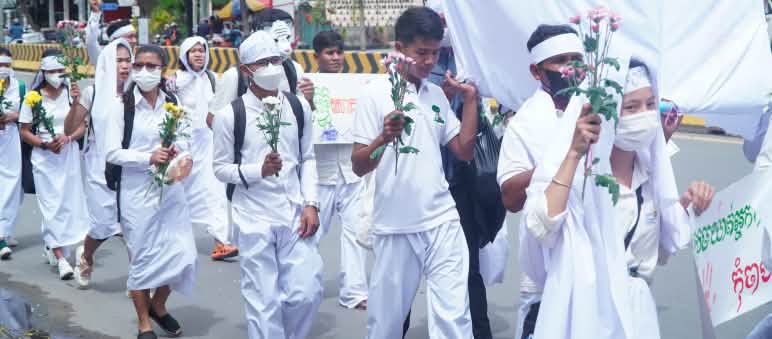 Jovens vestidos de branco correm com flores na mão por uma rua de Phnom Penh