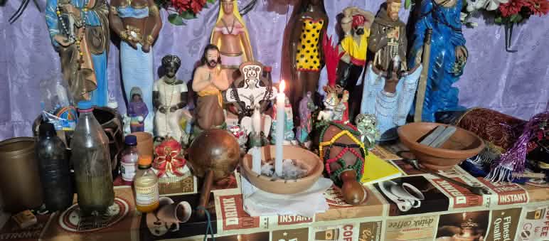 Altar com imagens de santos católicos e outras divindades, uma vela branca acesa ao meio