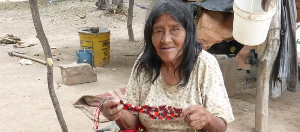 Mulher do povo Manjui sentada, trabalhando em um tecido à base de fibras vegetais