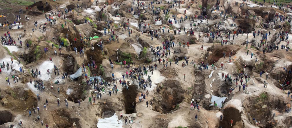 Vista aérea de buracos profundos, em parte preenchidos com água, e entre eles bastante gente.