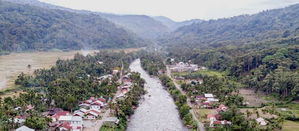 Rio passando pela aldeia com montanhas ao fundo