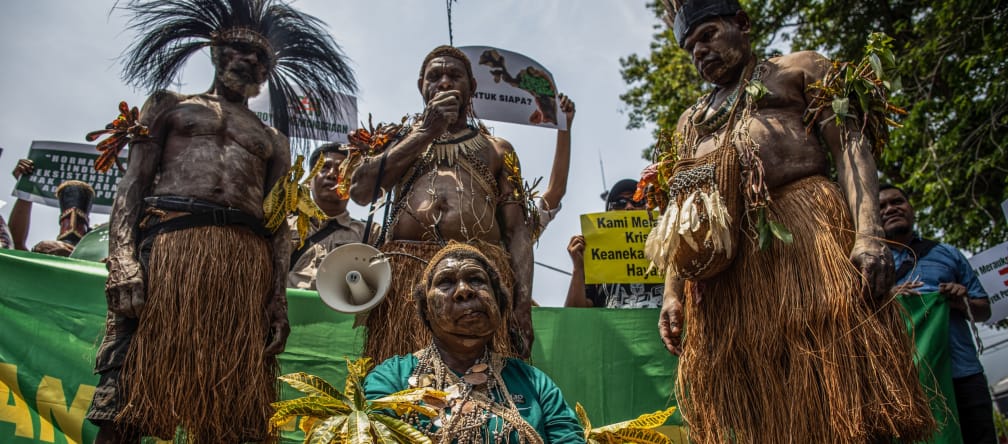 4 indígenas de Papua usando roupas tradicionais, diante de faixa