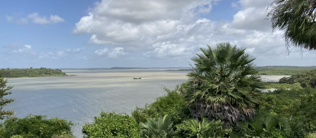 Vista de uma baía com vegetação ao fundo e nuvens brancas no céu