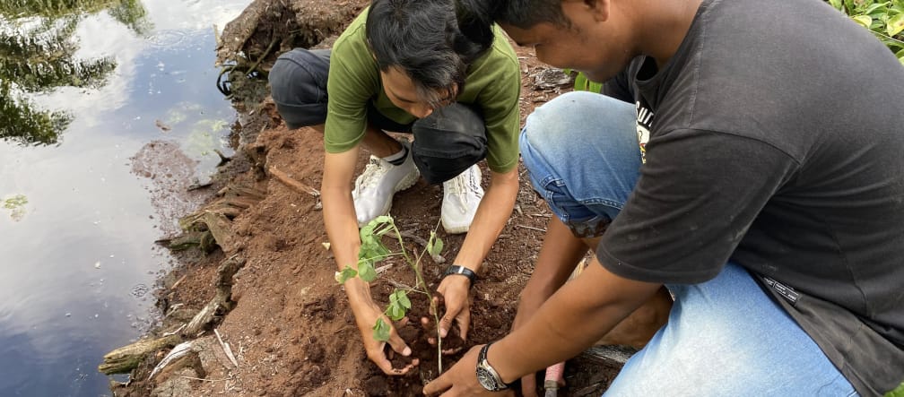 Dois homens plantando uma muda de árvore em um canal