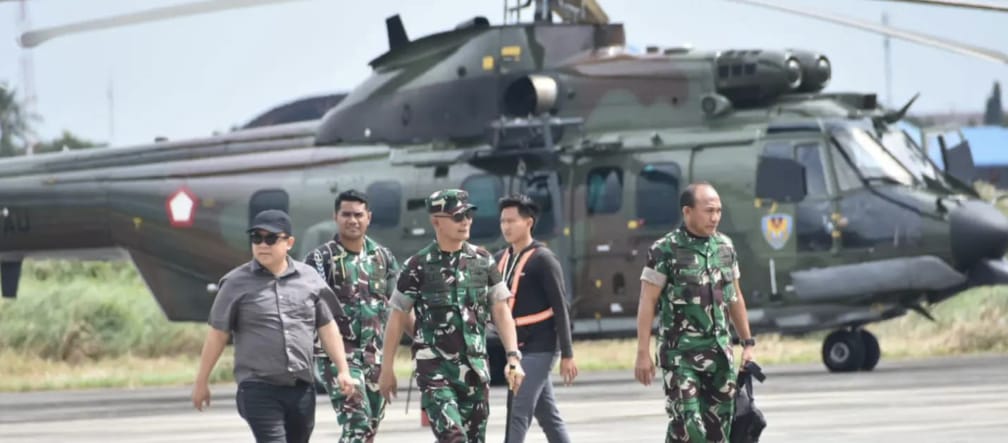 Três soldados e dois civis andando em frente de um helicóptero