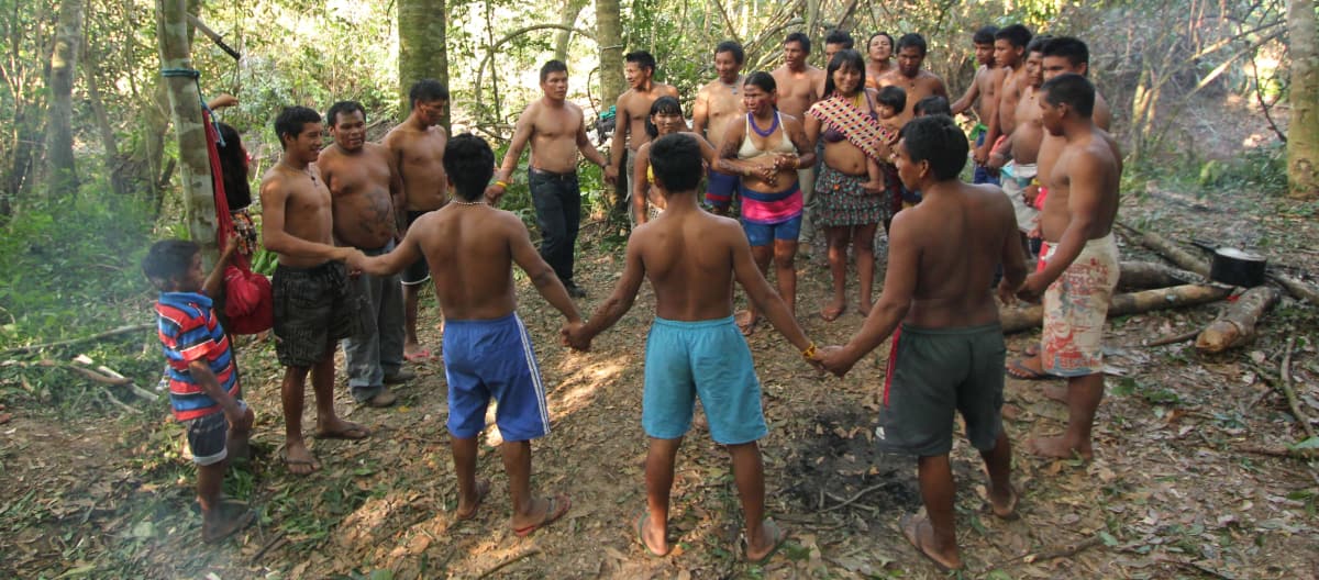 Indígenas Ka'apor - crianças, mulheres e homens - dão-se as mãos e fazem uma roda na floresta tropical