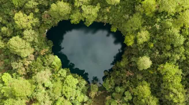 Foto aérea de um pequeno lago em forma de coração, cercado por densa floresta