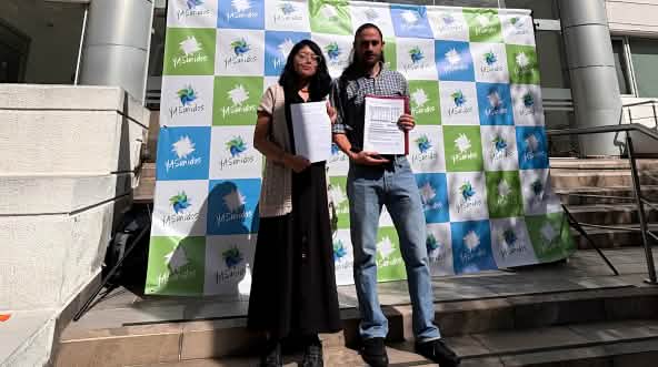 Uma mulher e um homem diante de tela com a inscrição “YASunidos”, em pé diante da entrada de um prédio, com documentos à mão.