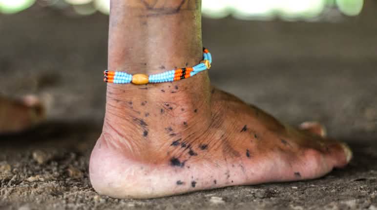 Pele marcada com grafismos feitos com tintura de genipapo Pé descalço traz desenhos feitos com tinta preta. No tornozelo, uma corrente feita de miçangas coloridas