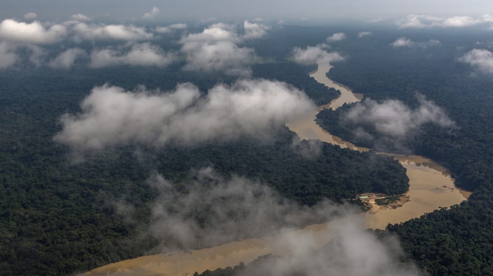 Fotografia aérea com nuvens e rio sinuoso passando pela floresta tropical