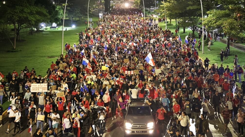 Manifestação com milhares de pessoas passando por uma rua na capital