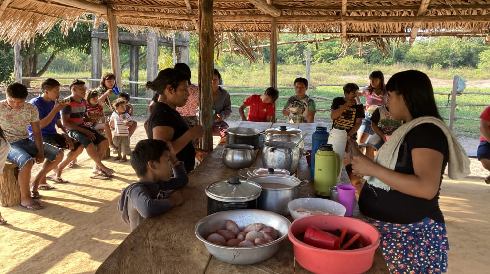 Mulheres indígenas, crianças e adolescentes em refeição comunitária em oca aberta
