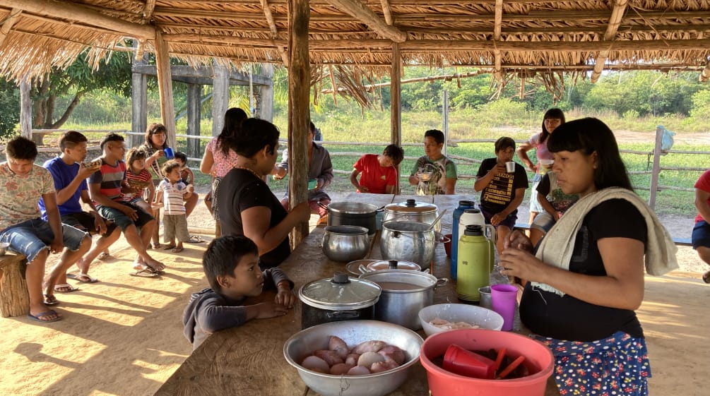 Mulheres indígenas, crianças e adolescentes em refeição comunitária em oca aberta