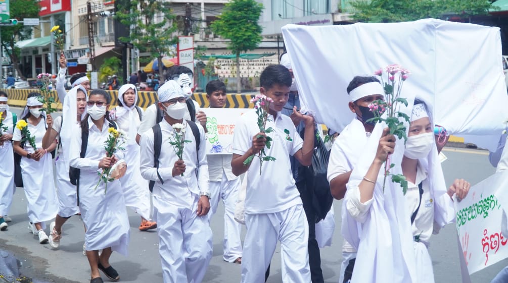Jovens vestidos de branco correm com flores na mão por uma rua de Phnom Penh